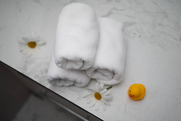 istock Soft Rolled Towels and a Rubber Duck With Daisies Arranged on a Marble Surface 2229894425