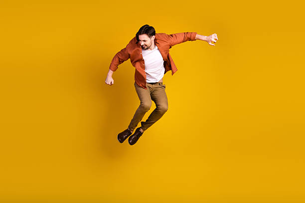 istock Dynamic young man in casual attire gracefully jumping against a vibrant yellow backdrop, exuding energy and confidence 2229896378