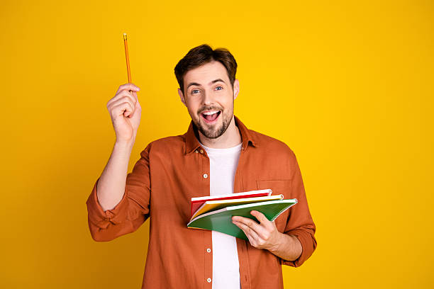 istock Cheerful young man with book and pencil on yellow background portraying learning and creative lifestyle 2229896445