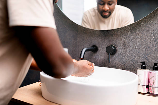 istock Man Washing Hands at Sink in Modern Bathroom Setting with Soap and Mirror 2229901146