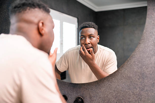 istock Man Looking in Bathroom Mirror Checking Face Thoughtfully in Bright Natural Light 2229901169