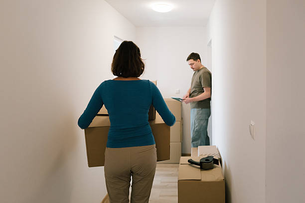 istock Relocation: A woman carries a box while a man connects to the internet using a touchpad. 2229901179