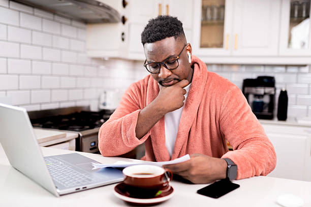 istock Man in Cozy Robe at Desk Reviewing Papers in a Modern Kitchen 2229903384