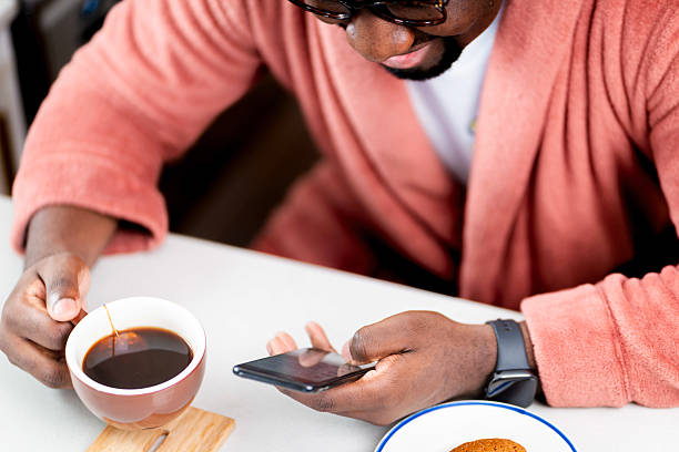 A man wearing a robe holds a cup of coffee and checks his phone while enjoying his morning routine in a cozy home environment.