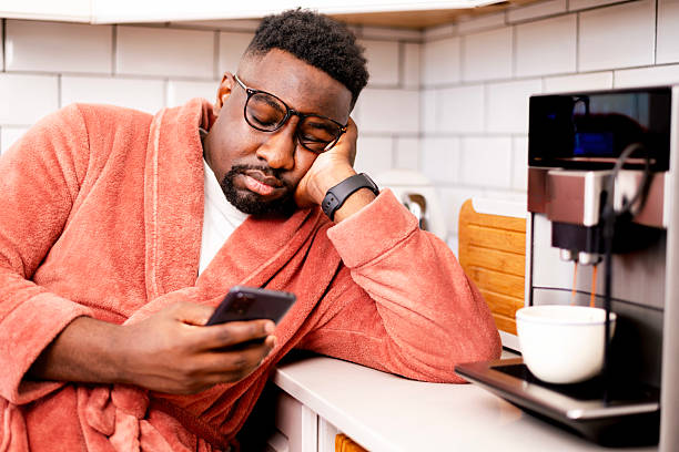 Man in Robe Relaxing with Smartphone Beside Coffee Machine in Kitchen