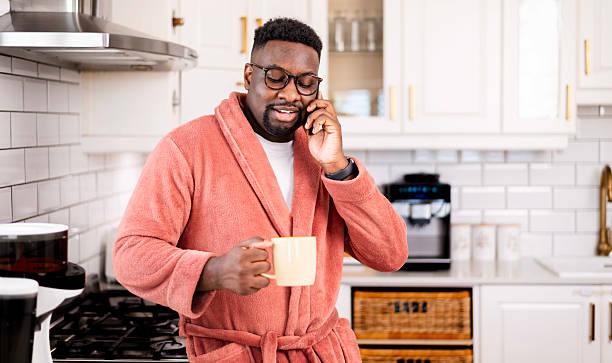 istock Man in Comfortable Robe Talking on Phone While Holding Coffee in Modern Kitchen 2229903428