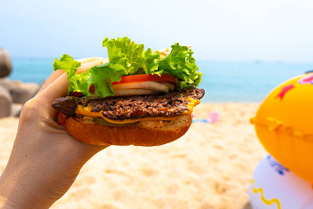 Woman holding burger in a hand against beach background