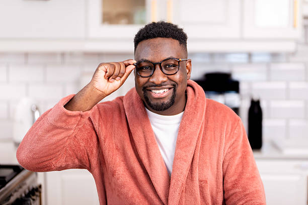 istock Smiling Man in Coral Bathrobe While Adjusting Glasses in a Kitchen 2229909507