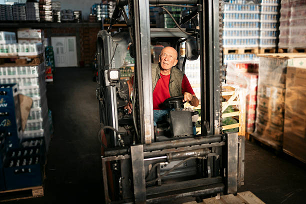 Senior warehouse worker driving forklift truck in large beverage distribution warehouse