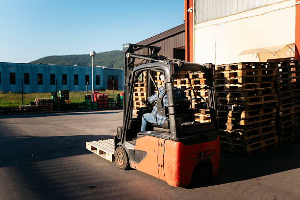 Warehouse worker driving forklift carrying wooden pallet in a depot