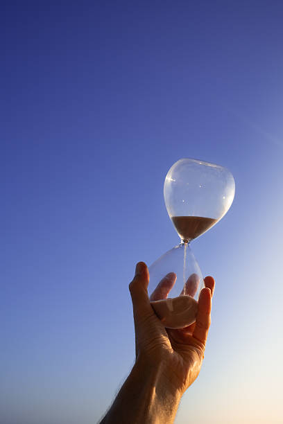 Hand holding an hourglass against a vibrant blue sky during sunset, capturing the essence of time's passage and the urgency of deadlines approaching