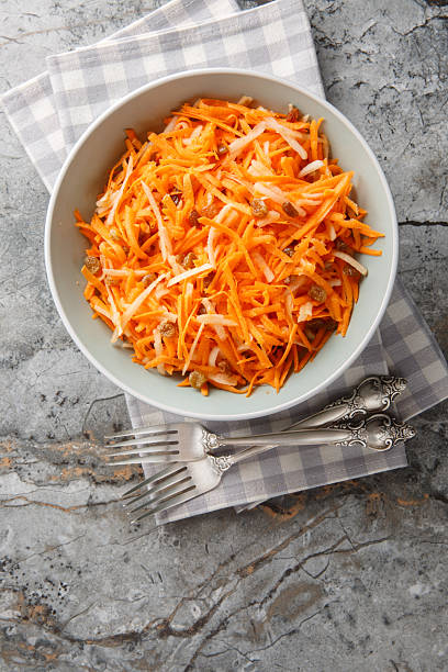 Raw carrot apple salad with raisins close-up in a bowl. vertical top view