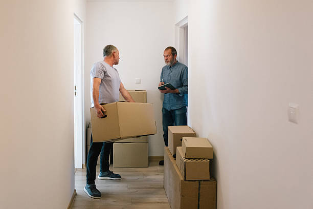 istock Moving: A man carry a box while another man tries to connect to the internet using a touchpad into an empty apartment 2229920834