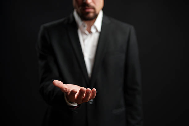 istock Businessman presenting an open hand against a dark background showcasing an invitation or offer 2229920864