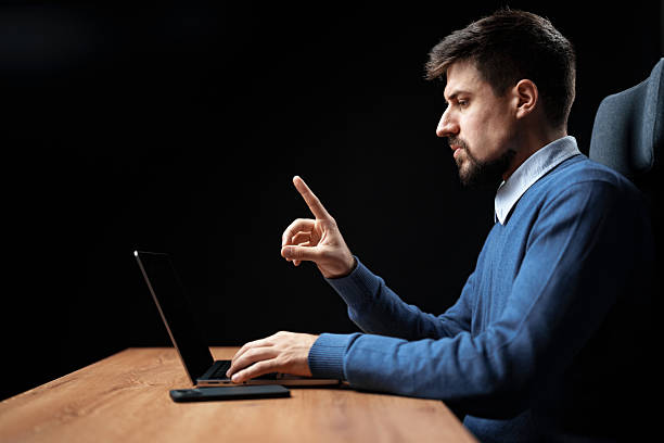 istock Man working intently on a laptop while gesturing in a dark office environment during evening hours 2229923080