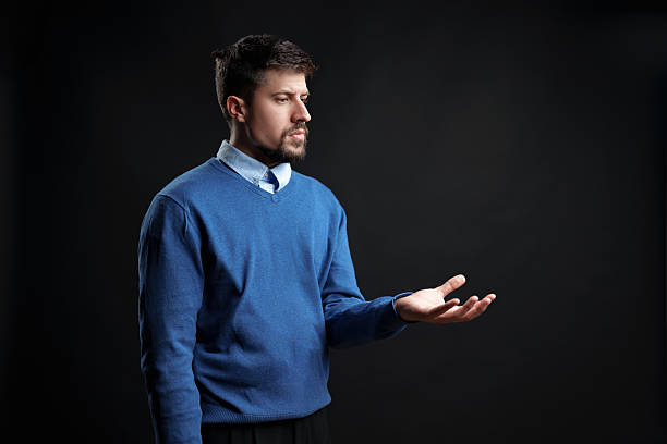 Man in blue sweater gestures thoughtfully in a dark setting conveying introspection and contemplation
