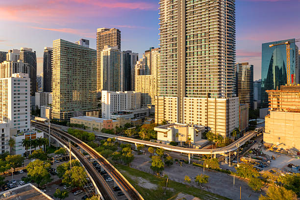 istock Public train system travels along elevated railroad in Miami downtown office district at sunset, with tall commercial and residential skyscrapers surrounding the tracks 2229925286