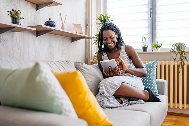 istock Mid-Adult Black Woman Using Digital Tablet While Sitting On The Sofa At Home 2229933022