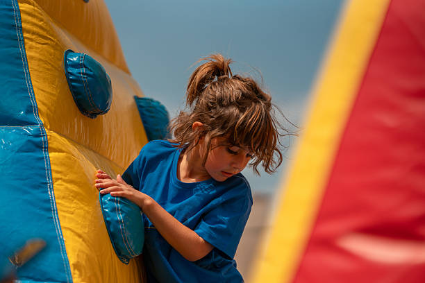 Girl climbing an inflatable wall at a vibrant summer event, relishing the joy of outdoor play and the excitement of active recreation
