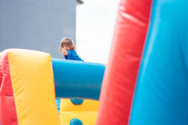 Young girl having fun and giving thumbs up while playing on a colorful inflatable bounce house at a summer event