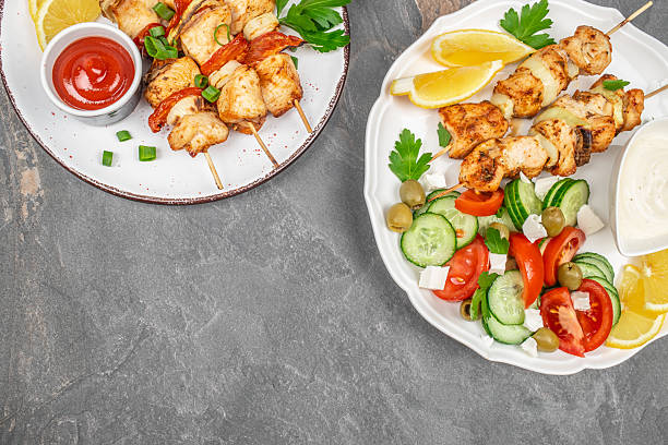 Grilled chicken skewers served with fresh salad, lemon wedges, and dipping sauces on rustic plates. copy space, top view