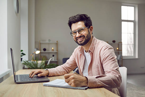 istock Smiling businessman sitting at desk with laptop computer 2229942677