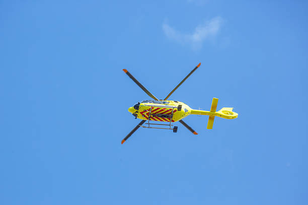 A bright yellow helicopter with distinct stripes hovers in the clear blue sky, showcasing its agile design against the expansive backdrop of daylight. The atmosphere is calm and serene.