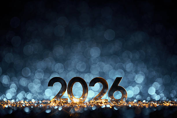 Sleek golden 2026 numbers rest on a shimmering surface, glowing against a dreamy backdrop of blue bokeh lights. A minimalist yet festive still life capturing the spirit of celebration and the beginning of a hopeful new year.