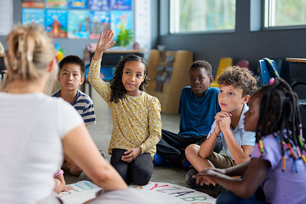 Young students attentively participate during a classroom lesson, with one raising their hand to answer. This image highlights diversity, cooperation, and an engaging learning environment in an elementary school.