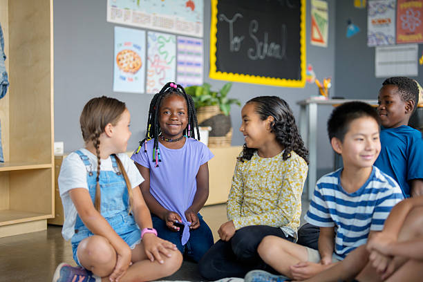Diverse children sitting together on the classroom floor, engaging in conversation and sharing ideas in a collaborative and friendly manner, surrounded by educational posters and supplies in a colorful room.