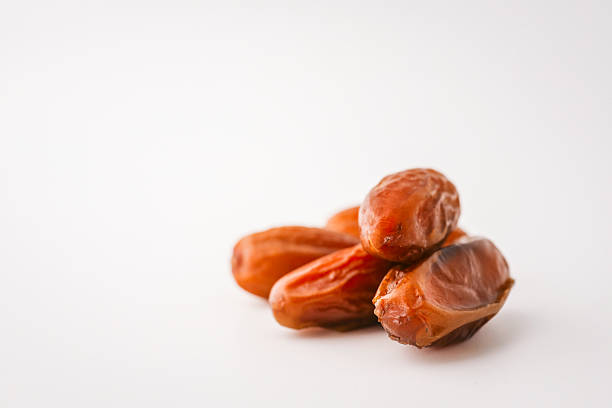 Top view of five dried dates arranged diagonally on a light cream background. Simple organic food layout, perfect for packaging, healthy eating, or clean food concepts.