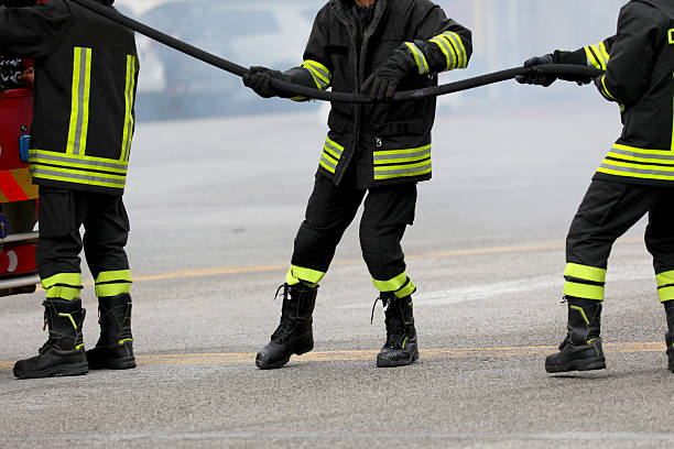 three firefighters wearing protective uniforms pulling a hose from a fire truck to run towards a fire