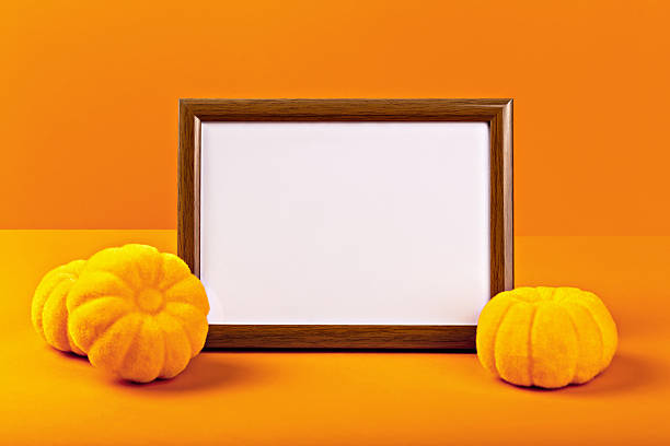 Halloween. Mockup. Vibrant orange background features an empty wooden frame surrounded by decorative yellow pumpkins, creating festive atmosphere perfect for Halloween celebrations and seasonal decor