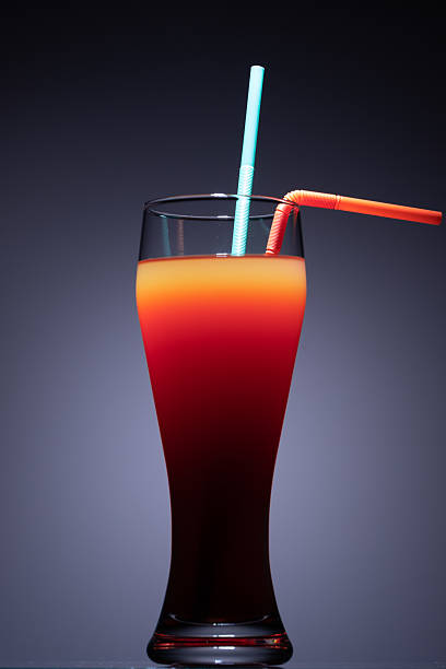 a tall glass containing a layered beverage, with distinct red orange and darker red brown layers