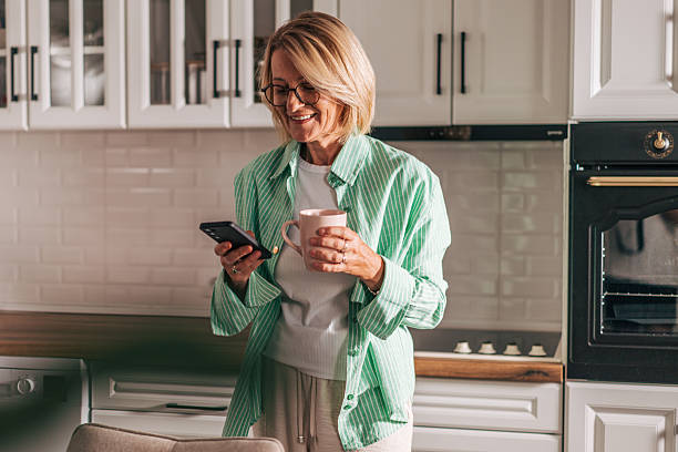 istock Senior woman enjoying coffee and using smartphone in kitchen 2229963218