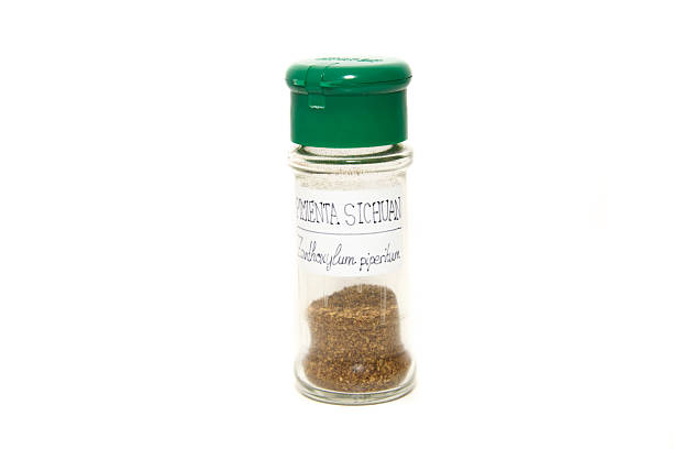 A clean, organized shot of several clear glass jars with lids, filled with various dried green herbs and black peppercorns on a white surface.