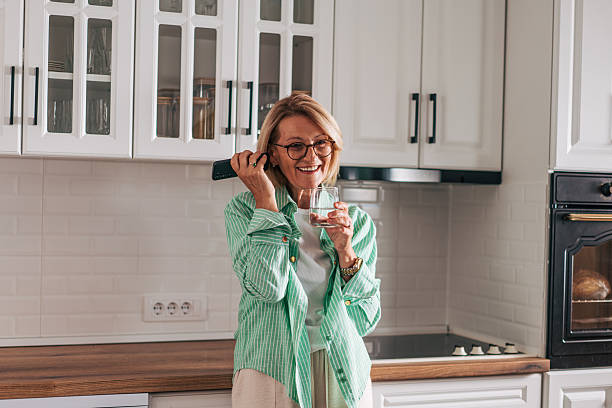 istock Senior woman talking on phone and drinking water in kitchen 2229964909