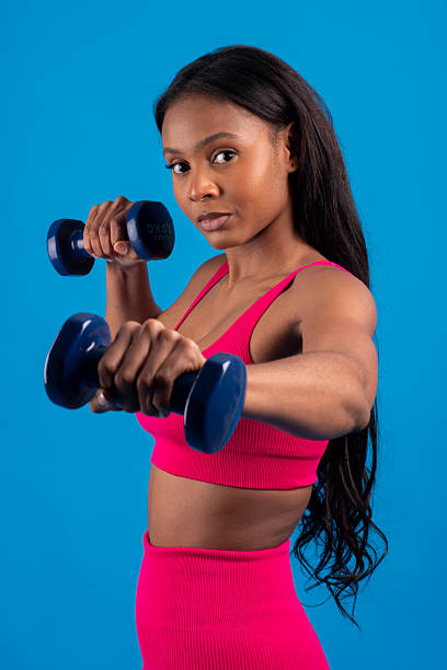 istock Young black woman lifting weights on blue background 2229973617