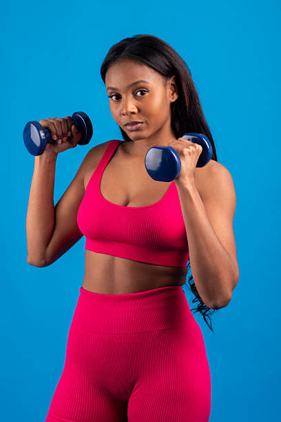 istock Young black woman lifting weights on blue background 2229974028