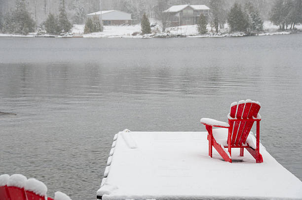 istock Red Adirondack chairs on a snowy dock during a winter snowfall 2229978710