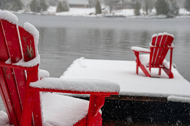 istock Red Adirondack chairs on a snowy dock during a winter snowfall 2229978739