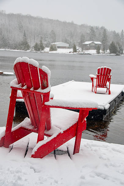 istock Red Adirondack chairs on a snowy dock during a winter snowfall 2229978751