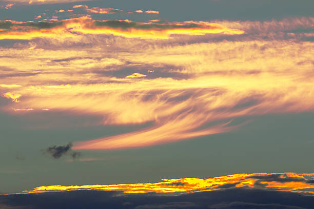 Swirls of vibrant colors dominate the sky during sunset, with golden hues blending into soft pastels. A mix of wispy and fluffy clouds adds depth to this tranquil evening atmosphere.