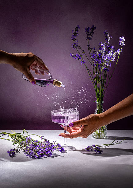 Hands pouring lavender syrup into elegant coupe glass with splash