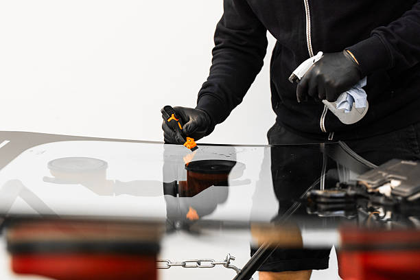 istock Technician scrapes and cleans new windshield after replacement to ensure perfect adhesion. Technician uses scraper to clean the surface of a new windshield post-replacement. 2229983498