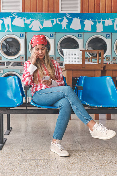 Woman watches clothes spin in a laundromat dryer, showcasing a typical laundry routine with a thoughtful expression