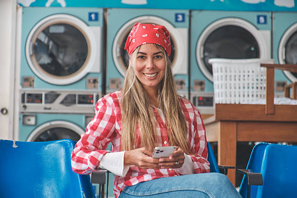 istock Woman using smartphone while waiting for laundry in laundromat 2229985819