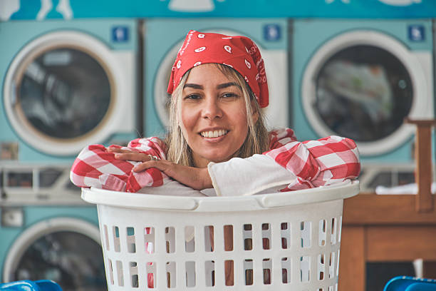 istock Laundromat worker smiling and leaning on laundry basket with washing machines in background 2229985843