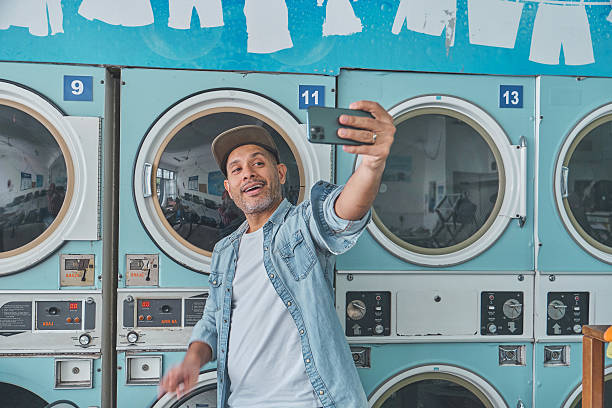 istock Stylish man taking a selfie at the laundromat while doing laundry 2229985959