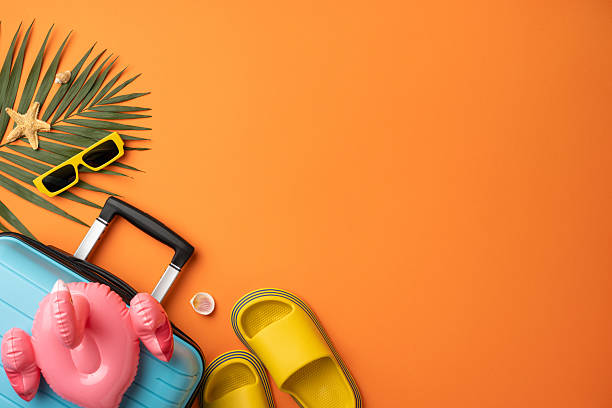 istock Bright and cheerful summer vacation-themed layout featuring a suitcase, slippers, sunglasses, and tropical decor on a vibrant orange backdrop 2229990272